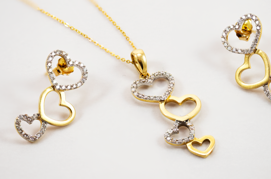 Parure collier et boucles d'oreilles dorés sertis de strass, avec motifs cœurs entrelacés.