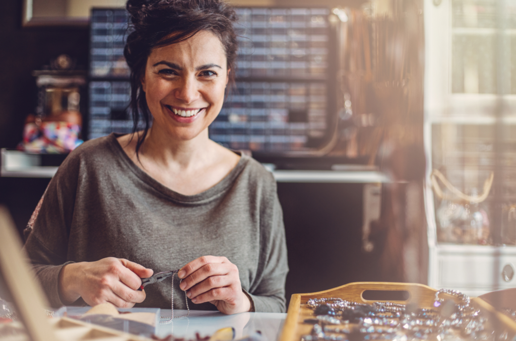 Femme souriante créant un bijou à la main dans son atelier