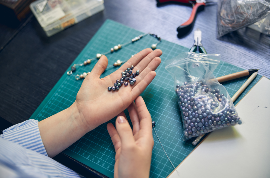 Main tenant des perles avec outils de création de bijoux DIY sur un plan de travail